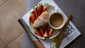 A cozy breakfast setup with croissant, strawberries, and coffee on a magazine.